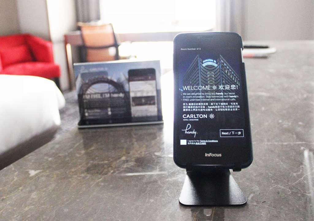 新加坡卡尔登酒店【Sg清洁认证】 客房 照片 The photo shows a smartphone set on a stand, displaying a welcome message in both English and Chinese. The phone appears to be part of a hotel service, likely providing information or functionality for guests. In the background, there is a small disp