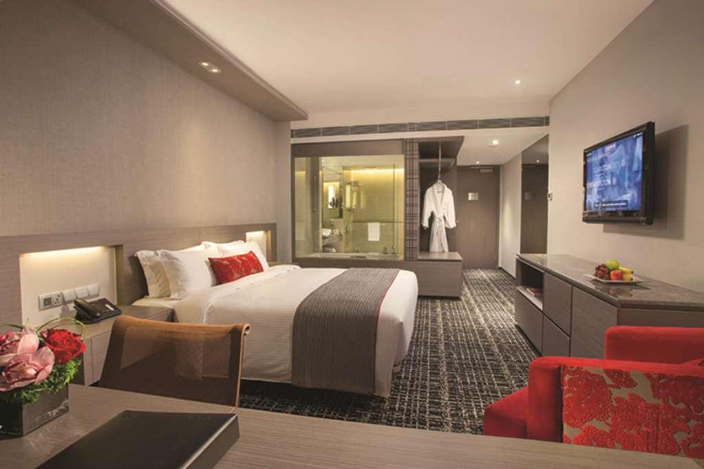 新加坡卡尔登酒店【Sg清洁认证】 客房 照片 The photo shows a modern hotel room featuring a neatly made bed with white bedding and red accent pillows. There's a contemporary desk with a black notepad in the foreground and a vibrant red chair beside it. A flat-screen television is mounted on th