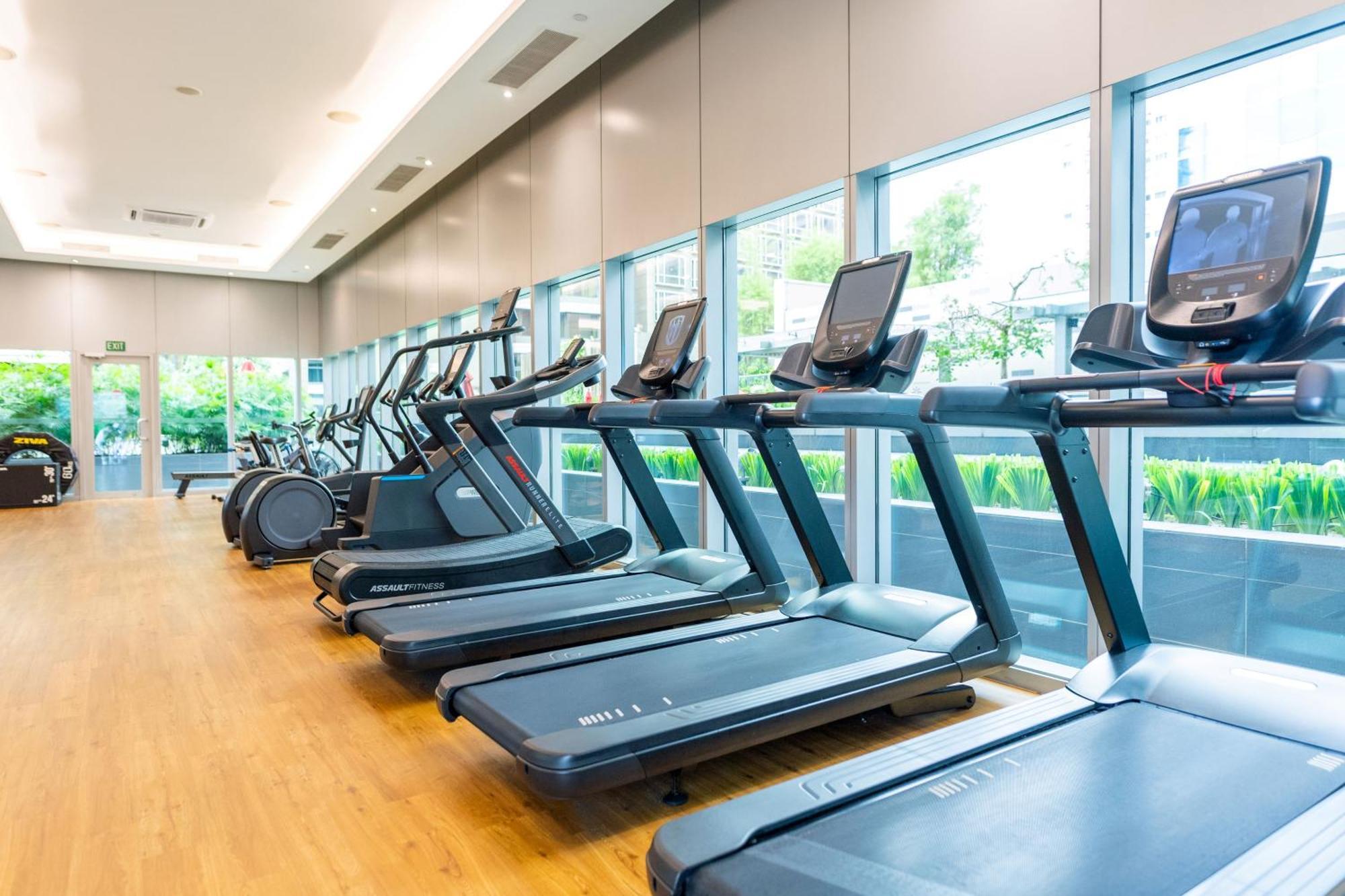 新加坡卡尔登酒店【Sg清洁认证】 外观 照片 The photo shows a modern gym facility featuring several treadmill machines lined up in a row. The treadmills are positioned on a wooden floor and have digital display screens. Large windows provide natural light and a view of greenery outside, creati